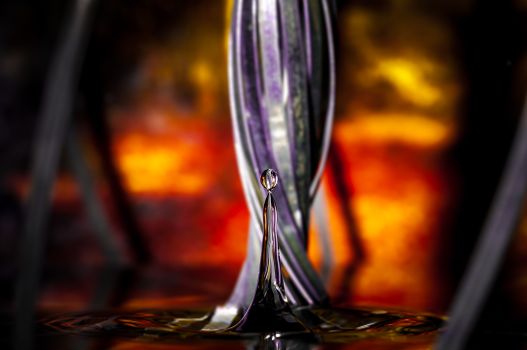 Colorful macro shot of a water drop with fiery bokeh background, showcasing abstract textures.