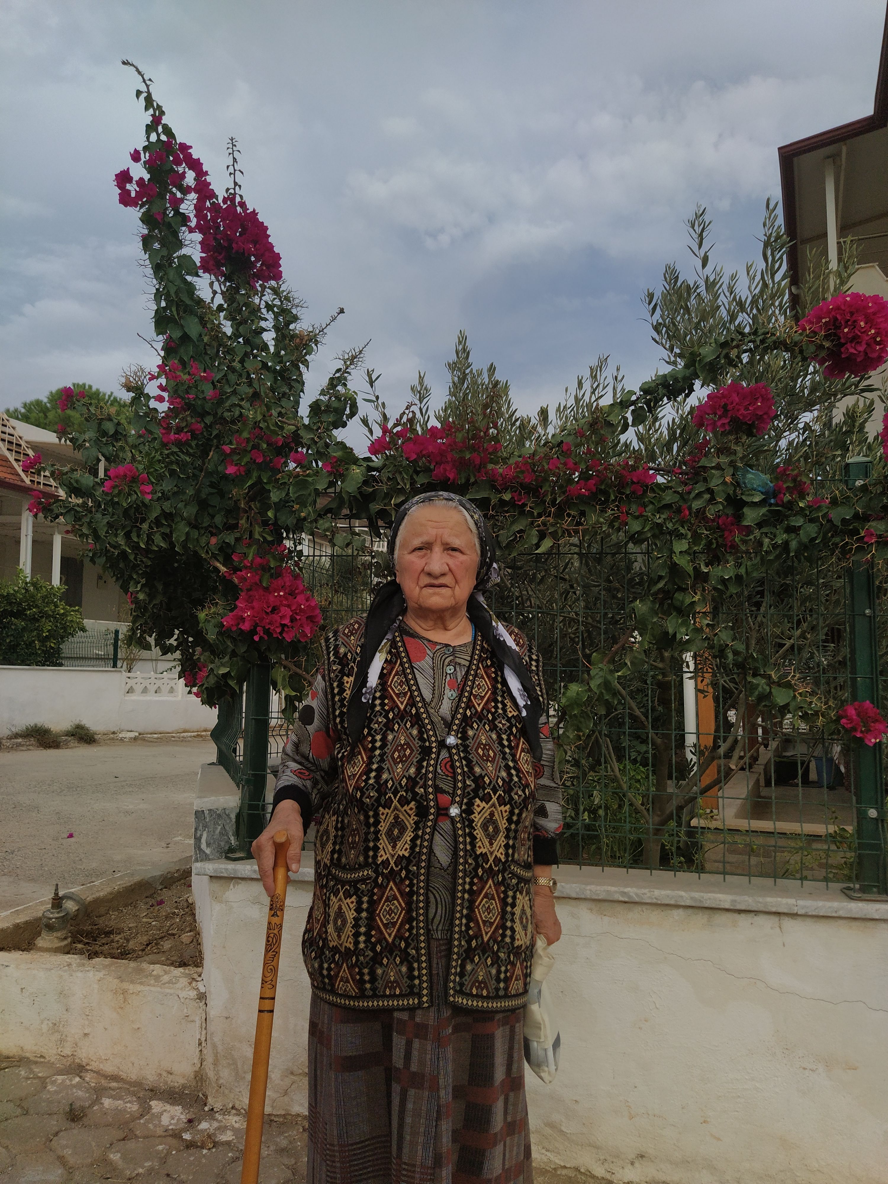 Senior woman with cane surrounded by flowers in Akbük, Turkey street view.