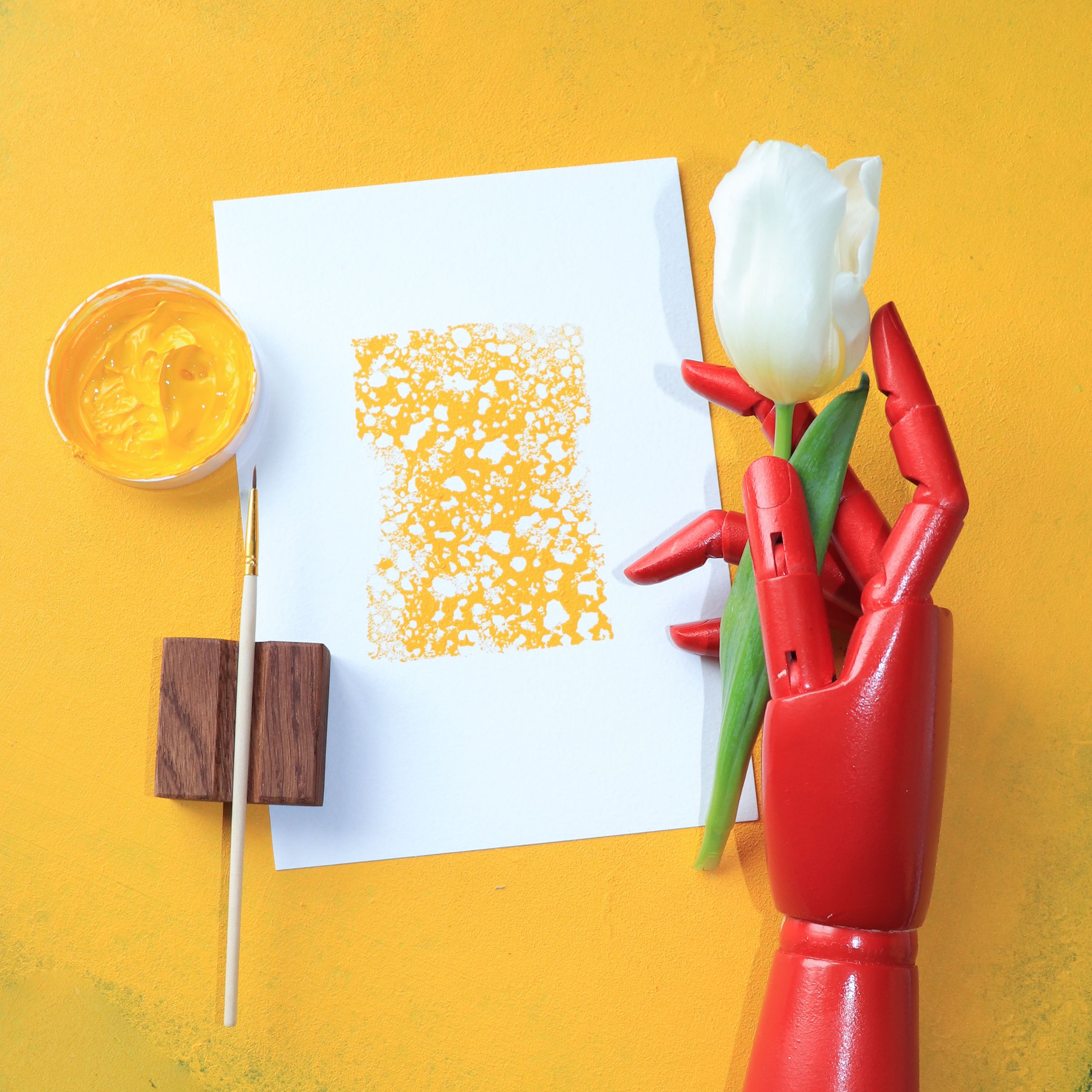 Overhead Shot of a Wooden Hand Holding a Flower beside a Painting