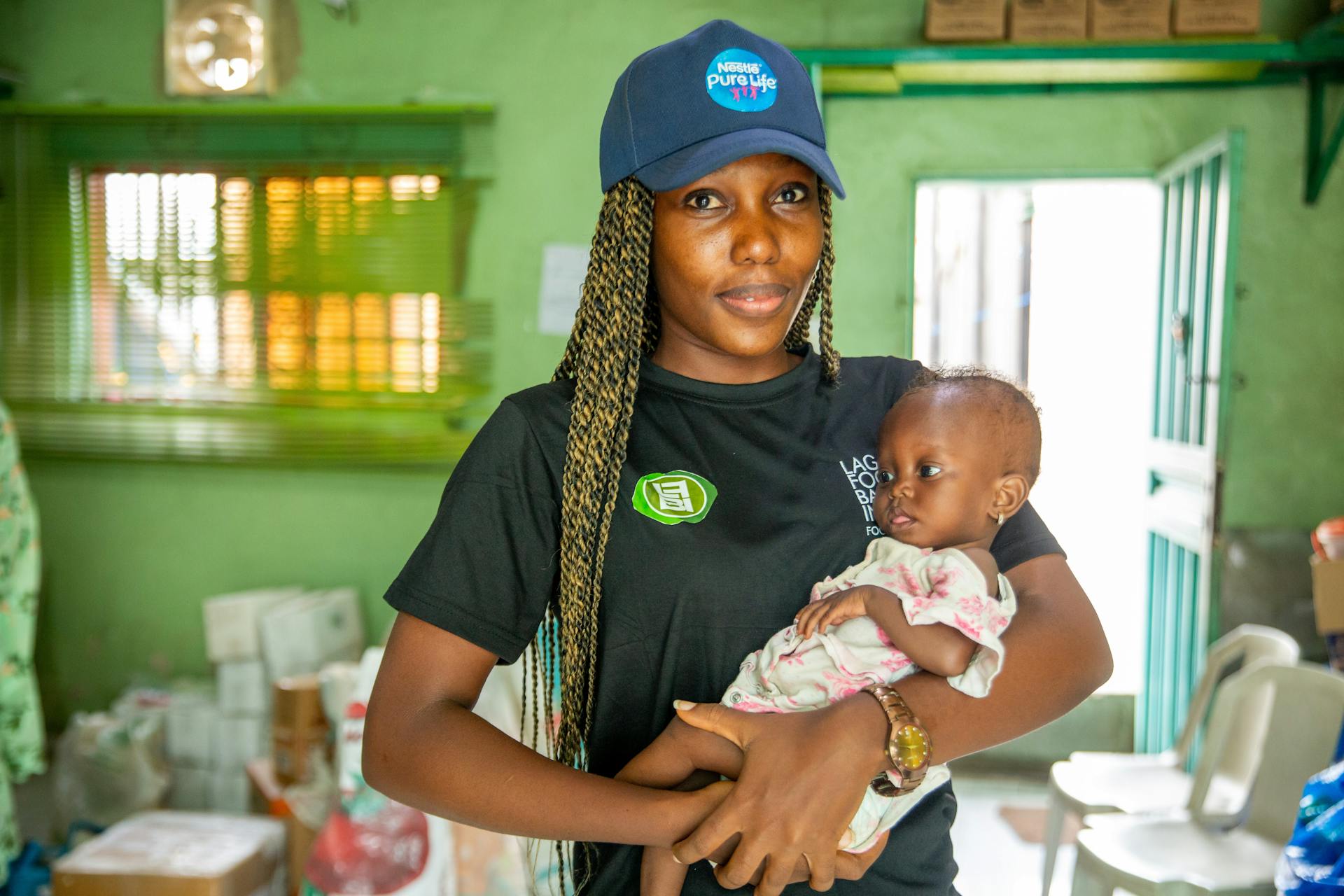 Smiling African woman volunteer holding a baby in a Lagos food bank setting.