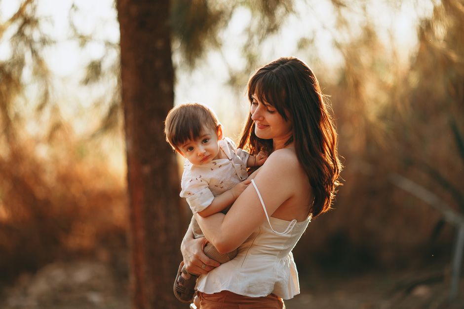 Una madre abraza a su hijo sonriente al aire libre bajo la cálida luz del sol, mostrando afecto y alegría.