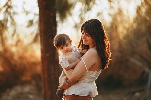 Free A mother embraces her smiling child outdoors in warm sunlight, showcasing affection and joy. Stock Photo