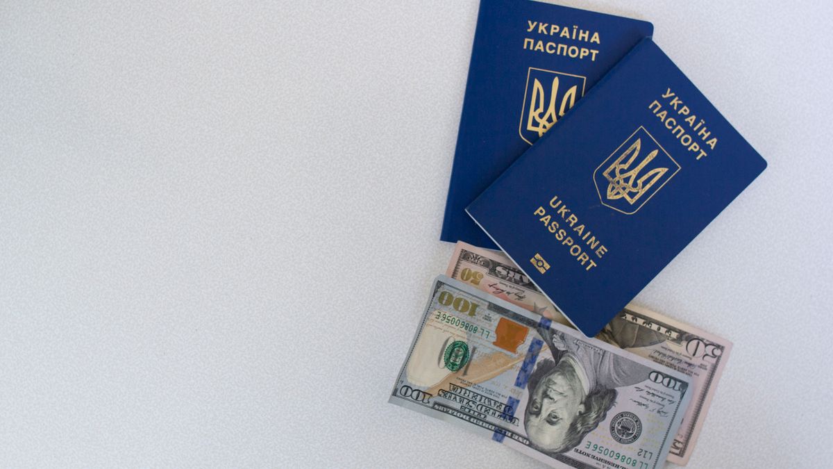 Top view of two Ukrainian passports with US dollar bills on a white surface.
