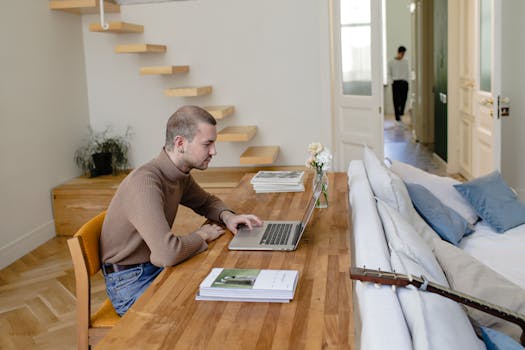 Man working on a laptop in a stylish, minimalistic home office with wooden decor.