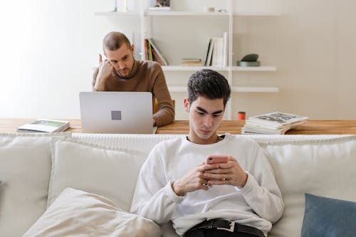 Man in White Sweater using Mobile Phone while Sitting on White Sofa
