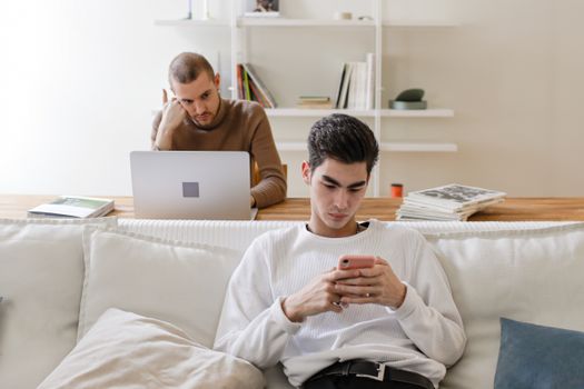 Two men in casual settings using a laptop and smartphone at home, working and relaxing.