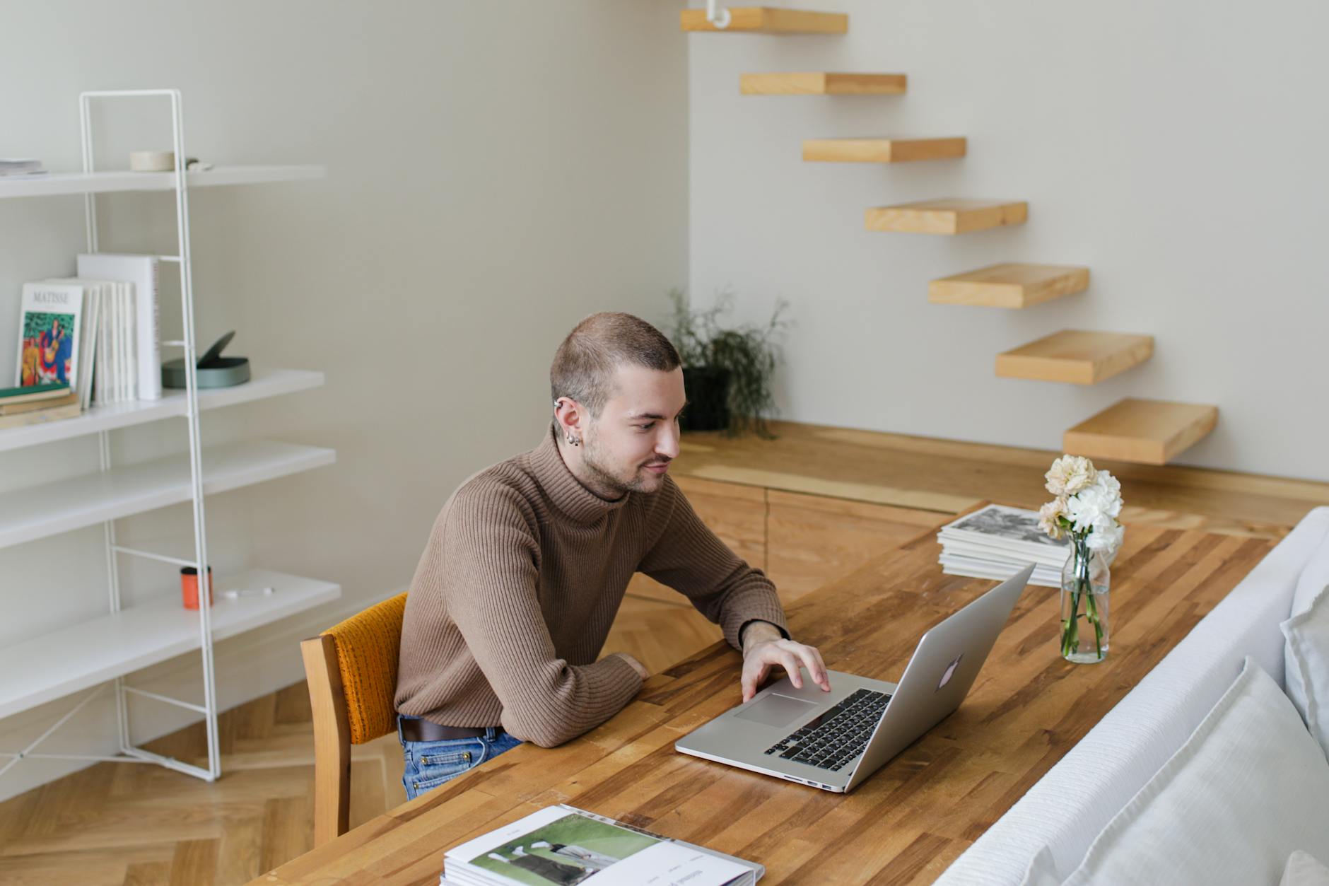 Young man working on a laptop in a stylish and modern living room office setup.