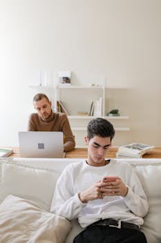 A modern indoor scene with two men using a laptop and smartphone in a minimalist living room.