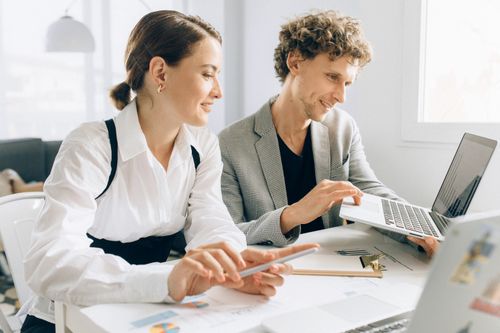 Free Two colleagues collaborating on a project, using laptops and documents in a modern office setting. Stock Photo