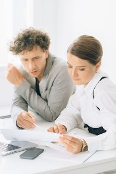 Two colleagues engaged in a discussion about documents in a bright office setting.