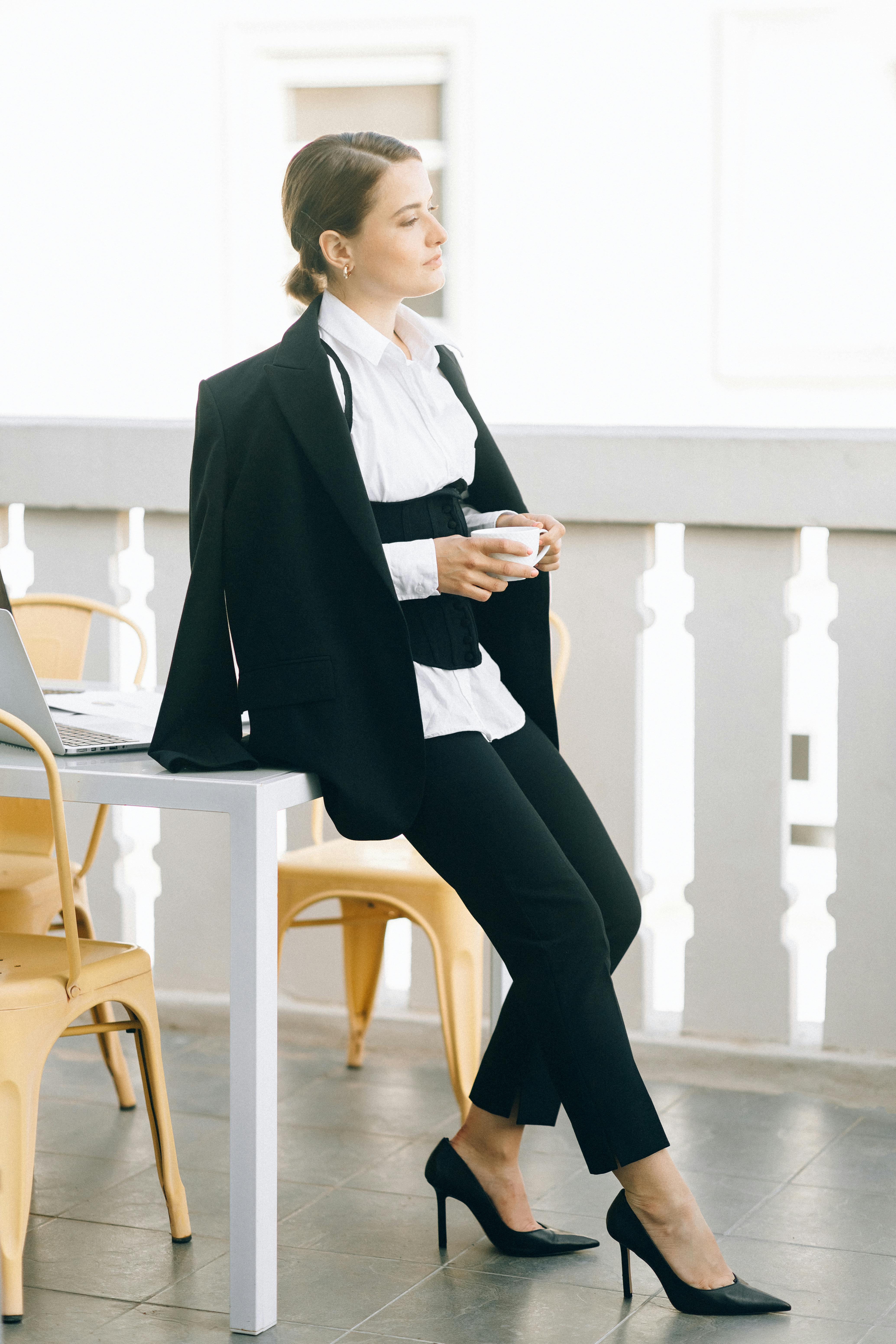 a woman in black blazer and black pants sitting on a white wooden table