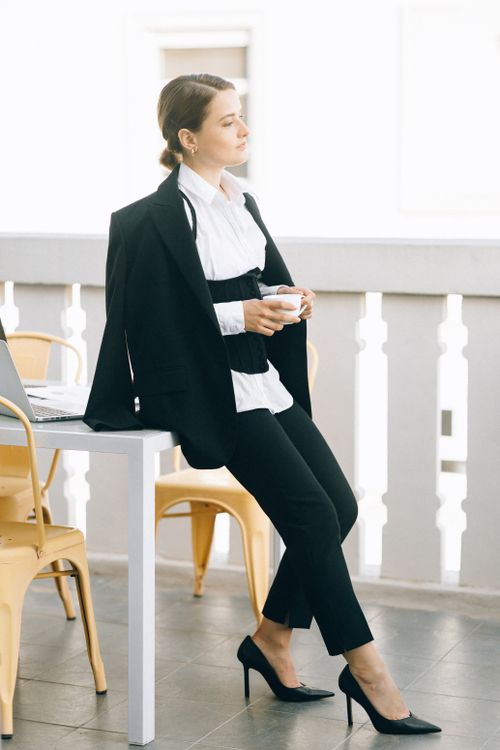 Free Professional woman in corporate attire enjoying coffee on an outdoor balcony. Stock Photo