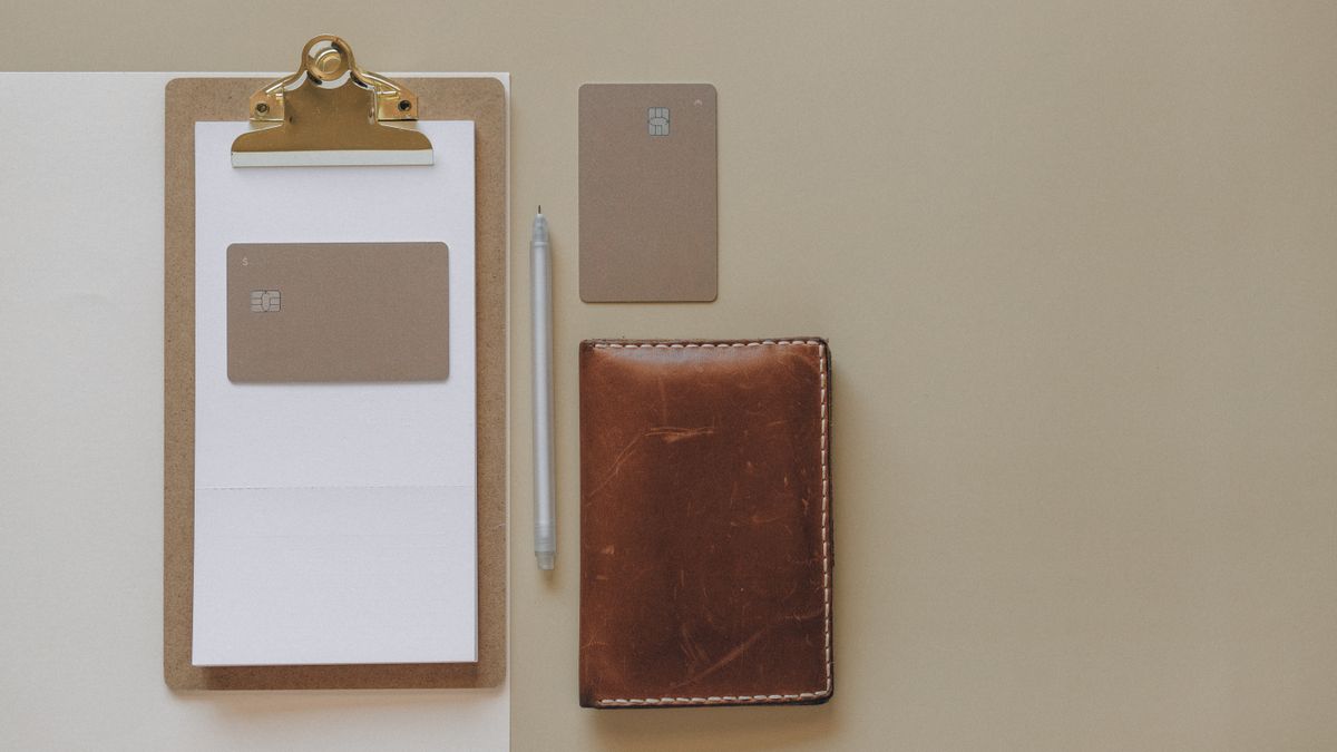 Flat lay of a minimalist office desk with clipboard, credit cards, pen, and leather wallet.