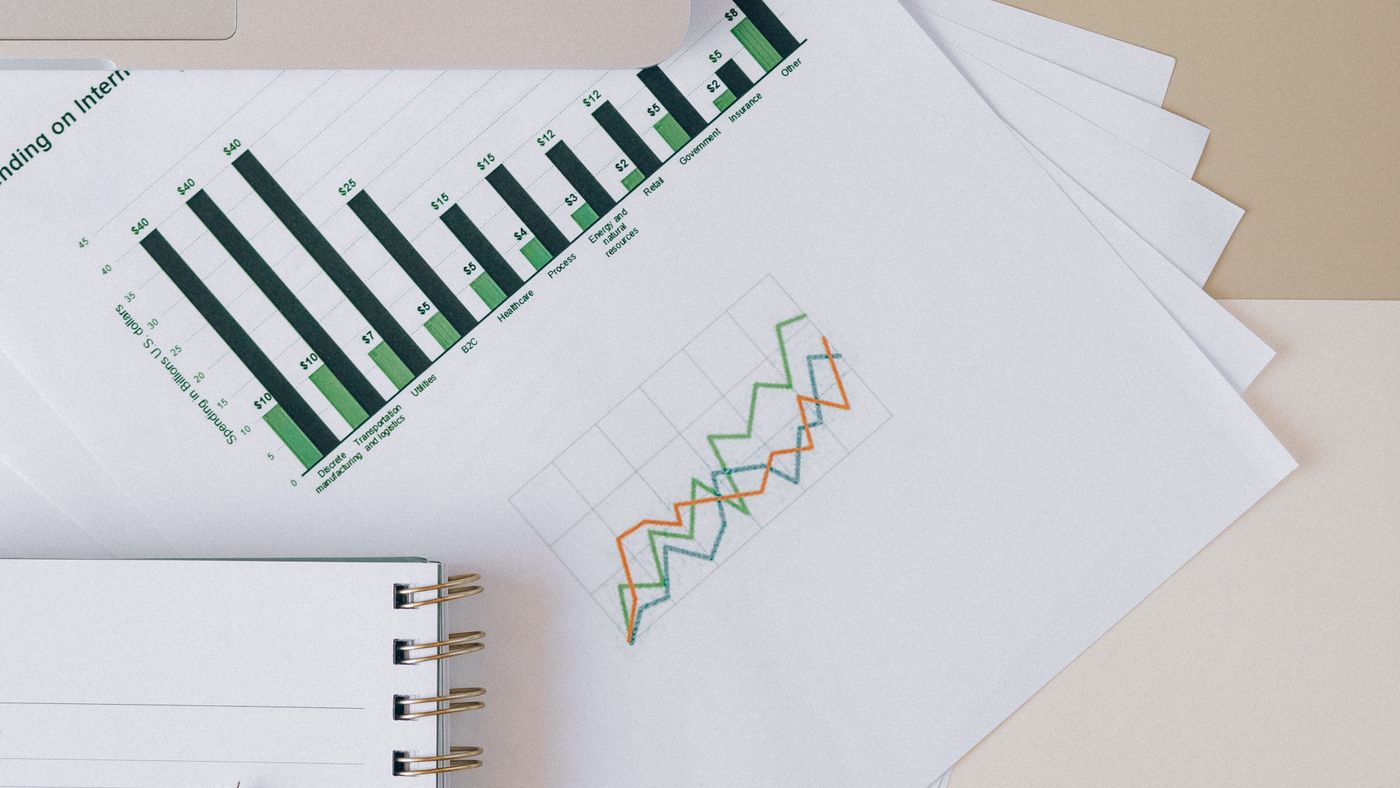 Check the underlying values before using a converted report. Photo: Nataliya Vaitkevich / Pexels; illustrative charts, not measured Excel results. Printed green bar charts and line graphs beside a spiral notebook