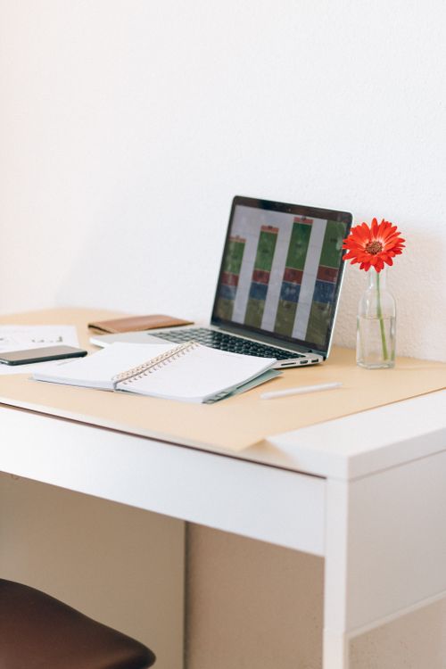 Free Modern home office desk with a laptop, notebook, and flowers, creating a minimalist workspace. Stock Photo