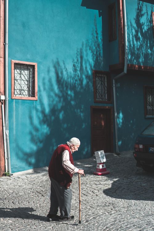 Free Side view of elderly man walking with cane on pavement near blue building wall in town Stock Photo