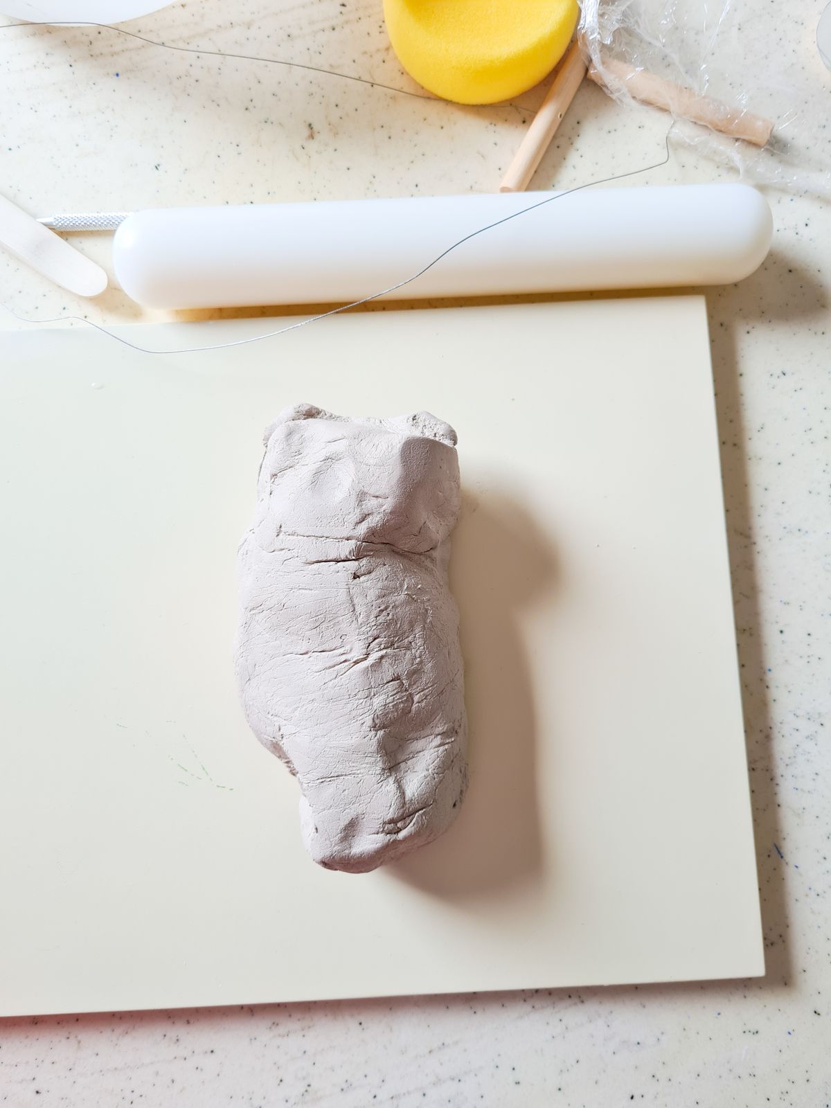 Clay sculpting tools beside a small handmade clay figure on a work table