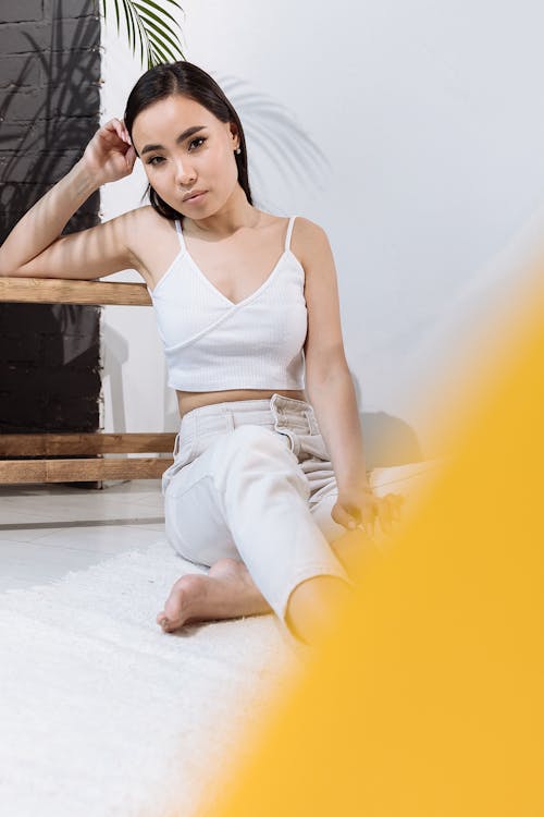 Stylish Woman in White Tank Top and White Denim Jeans Sitting on Floor