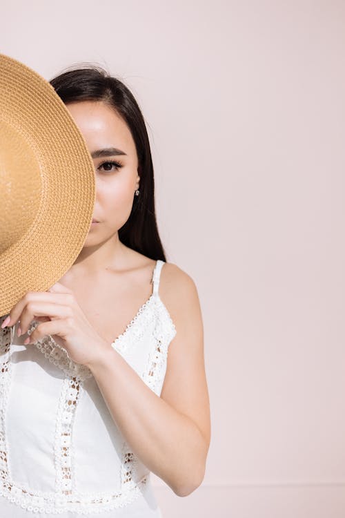 Free Woman in a White Dress Covering Half of Her Face with a Hat Stock Photo