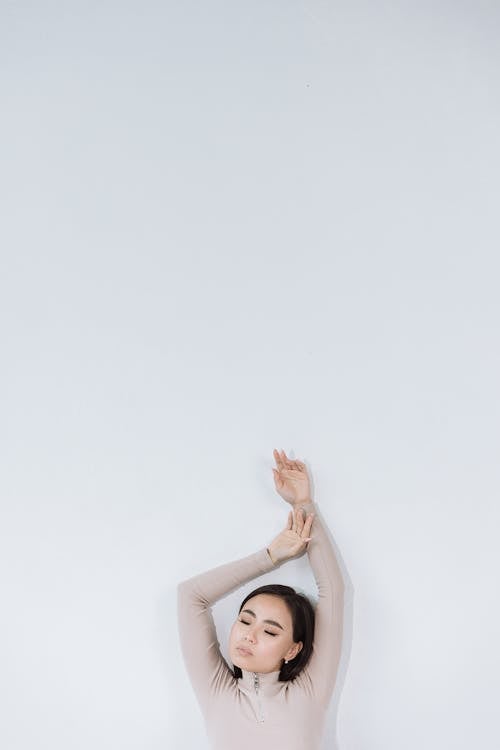 Free Woman in a Beige Turtleneck Posing with Her Hands Above Her Head Stock Photo