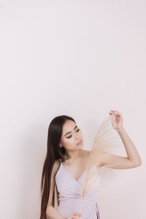 Free A serene portrait of an Asian woman holding pampas grass with a neutral background. Perfect for lifestyle and fashion themes. Stock Photo