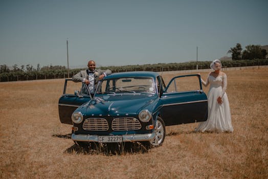 A stylish couple poses with a classic car in an outdoor wedding photoshoot.