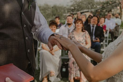 A close-up of a couple exchanging rings during an outdoor wedding ceremony, symbolizing love and commitment.