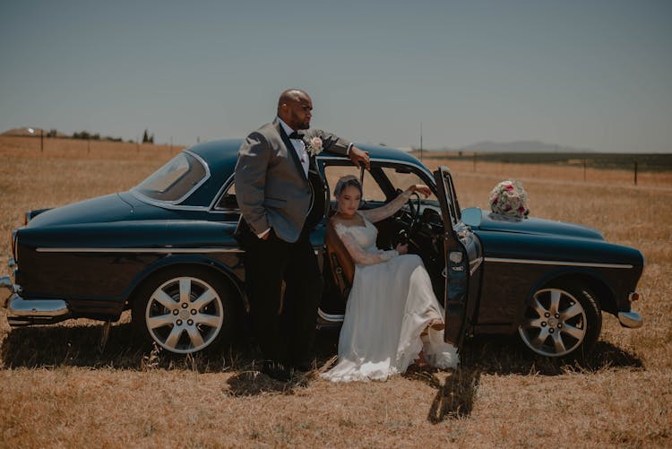 Newlyweds Posing With Car On Field