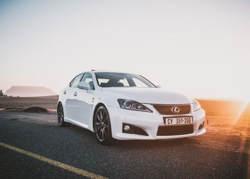 A sleek white sedan parked on an open road with a dramatic sunset and clear sky.