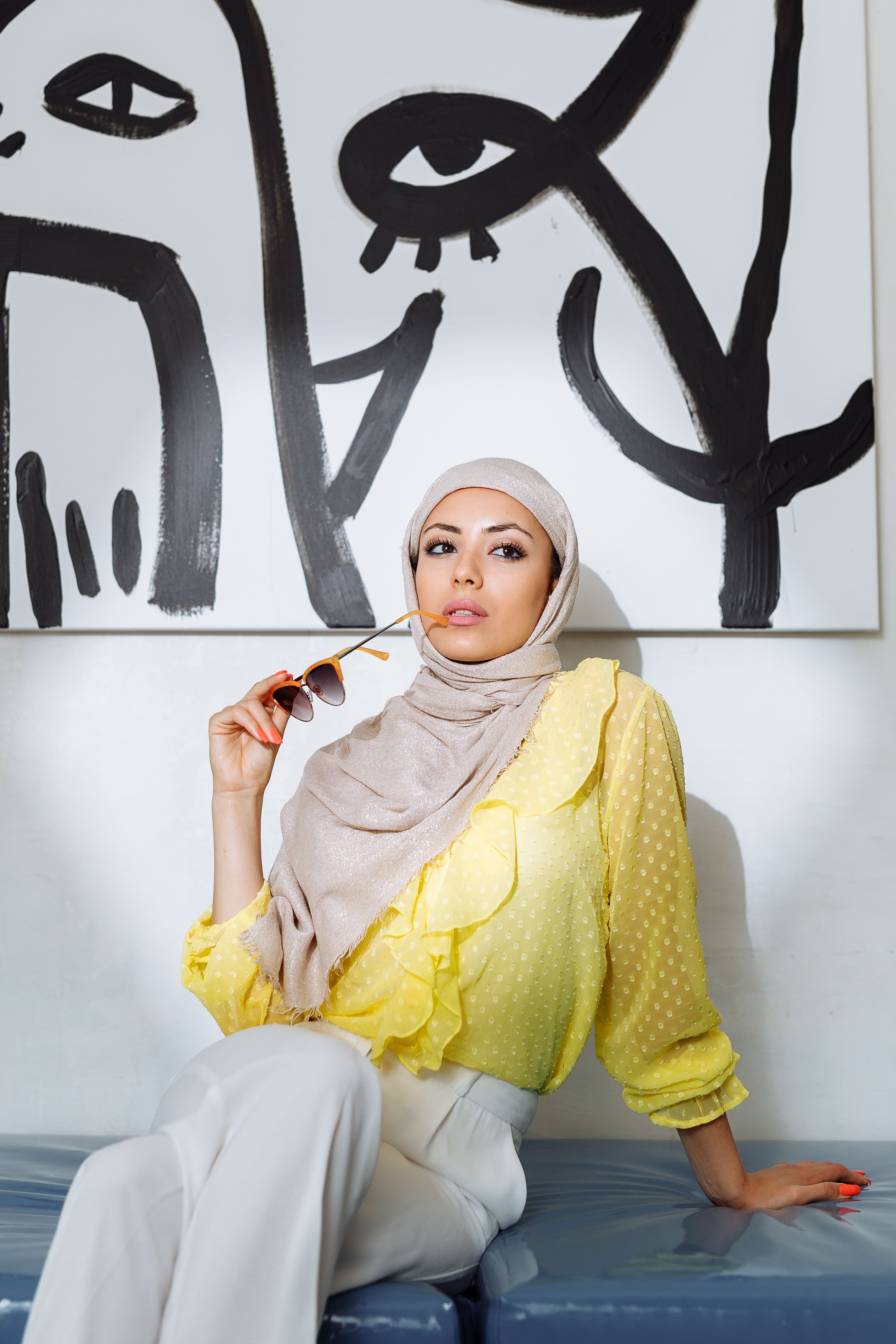 Chic woman wearing hijab and yellow top posing in a contemporary art-filled space.