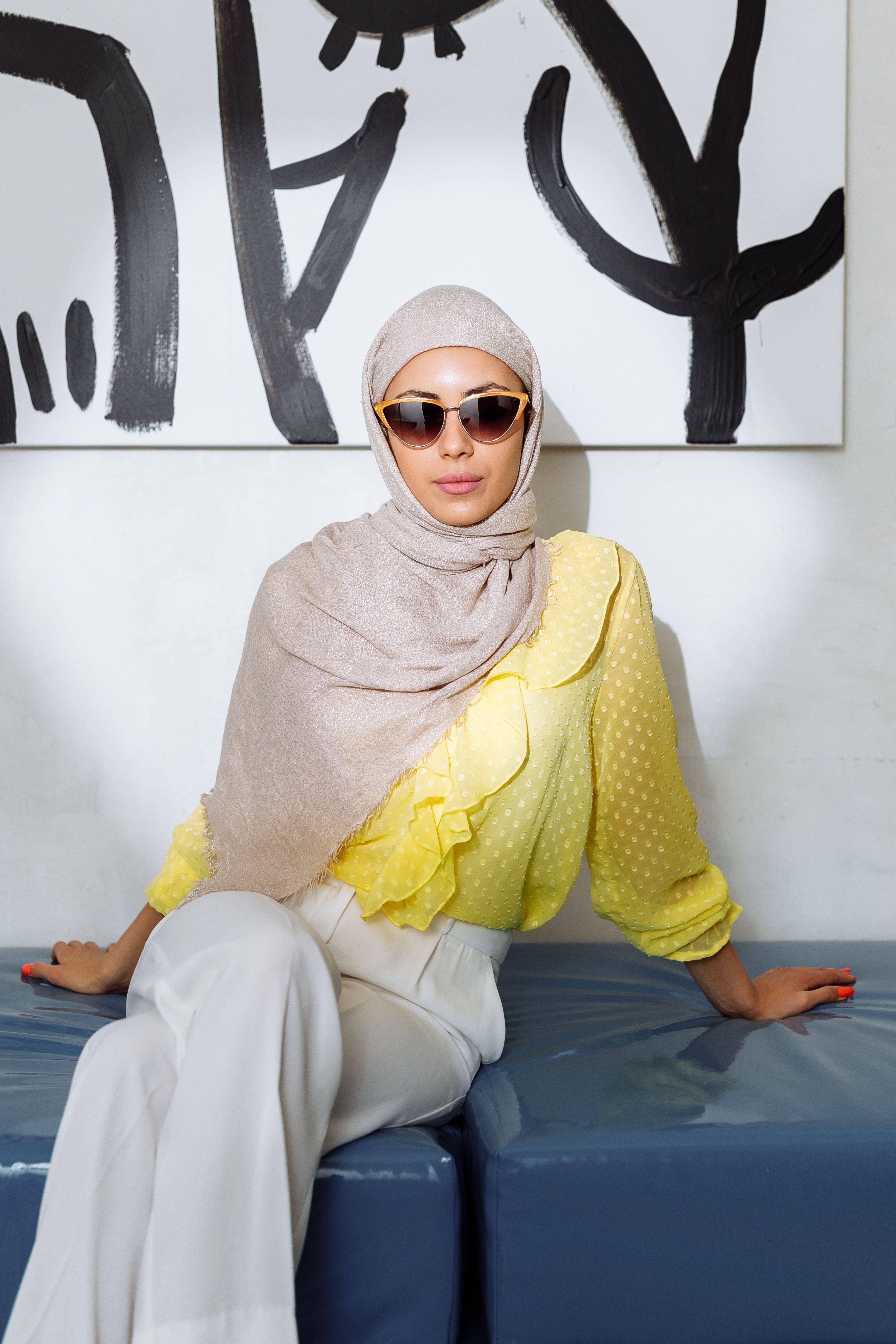 Modern woman wearing a hijab and sunglasses, seated indoors in a stylish setting.