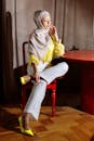 Woman in Yellow Long Sleeve Shirt and White Pants Sitting on Red Chair