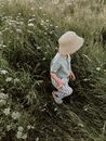 From above of unrecognizable child in casual clothes and hat walking on grassy meadow with white flowers on summer day