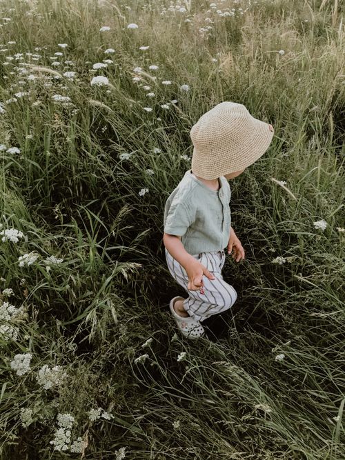 Free From above of unrecognizable child in casual clothes and hat walking on grassy meadow with white flowers on summer day Stock Photo