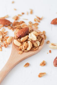 Close-up of a wooden spoon with granola, almonds, and peanuts on a white background.