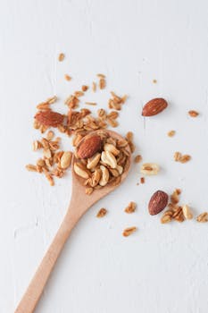 Close-up of granola and mixed nuts on a wooden spoon over a white background, perfect for food concept.