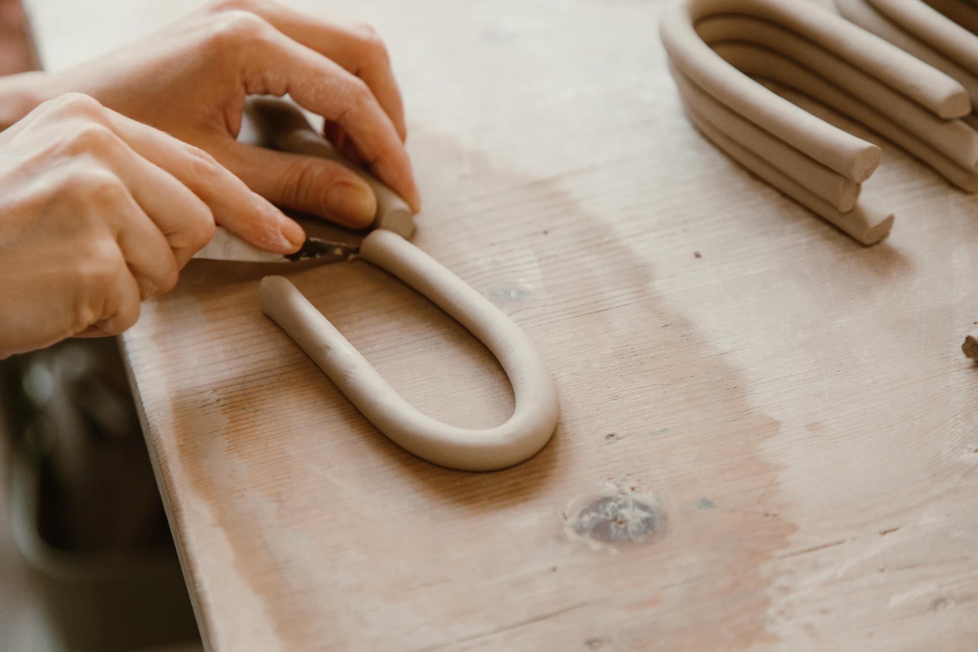 A Person Cutting a U Shaped Clay on a Wooden Surface