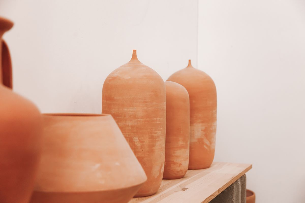 Raw terracotta bud vases lined up on a studio shelf