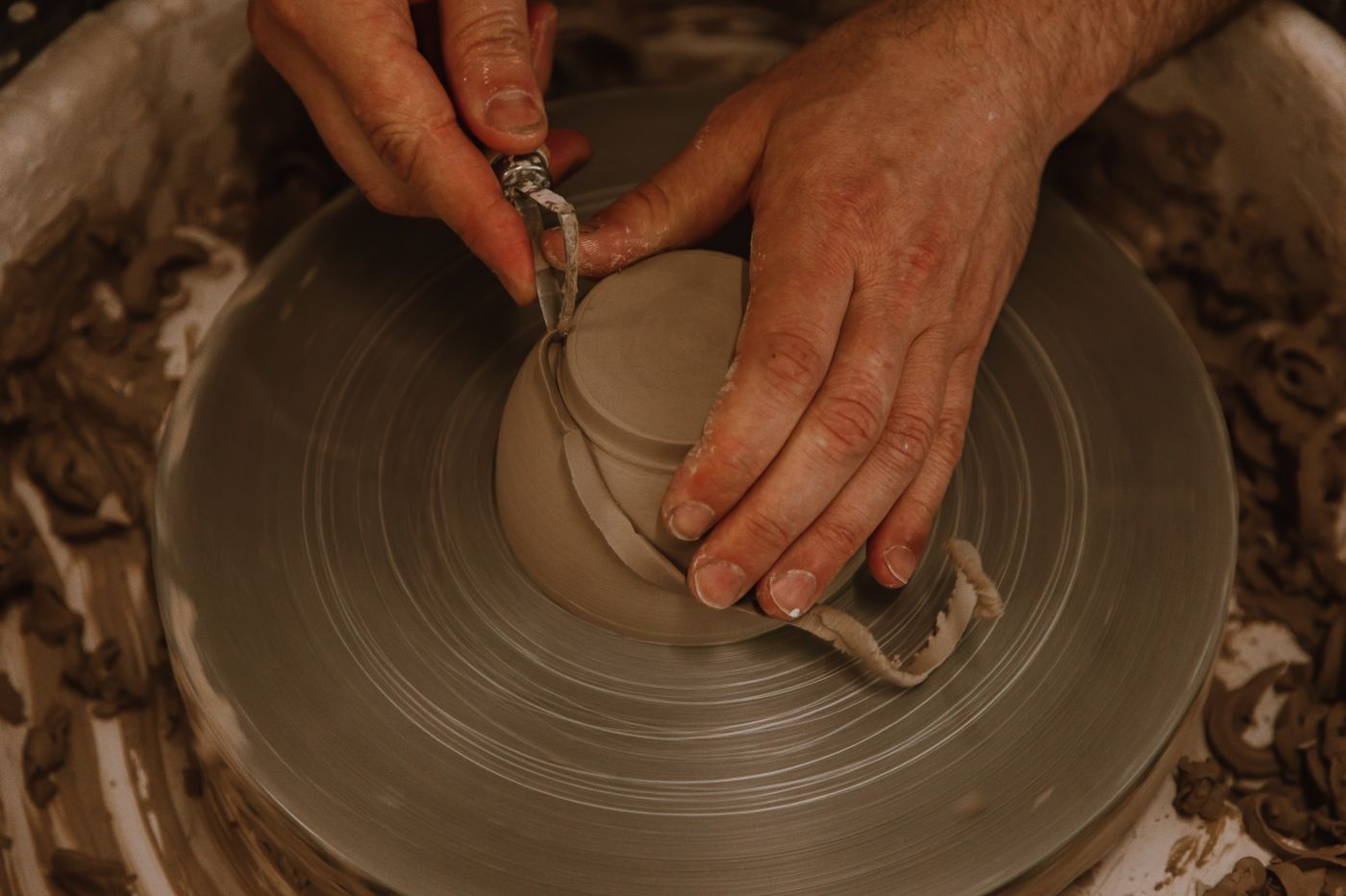 Hands shape wet clay on a spinning pottery wheel, forming a rounded vessel.