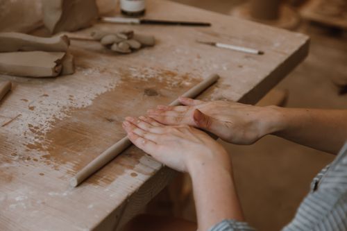 Free A woman skillfully rolling clay on a wooden table, focusing on her hands. Stock Photo