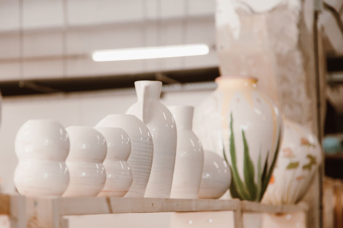 Glazed white vases and jugs lined up on a pottery studio shelf