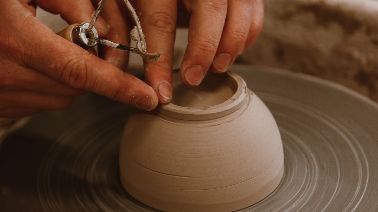 Close-up of hands shaping wet clay into a bowl on a pottery wheel, an illustrative real photo with no faces in the frame, chosen for the Clayface story
