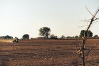 Tractor working on open field with clear sky and trees in rural setting.