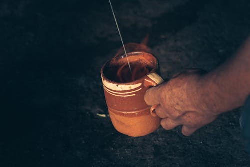 Person Holding a Brown Ceramic Mug with Flame