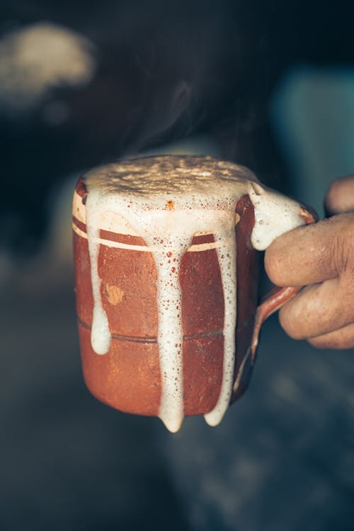 Hand Holding a Brown Mug with Foamy Liquid 