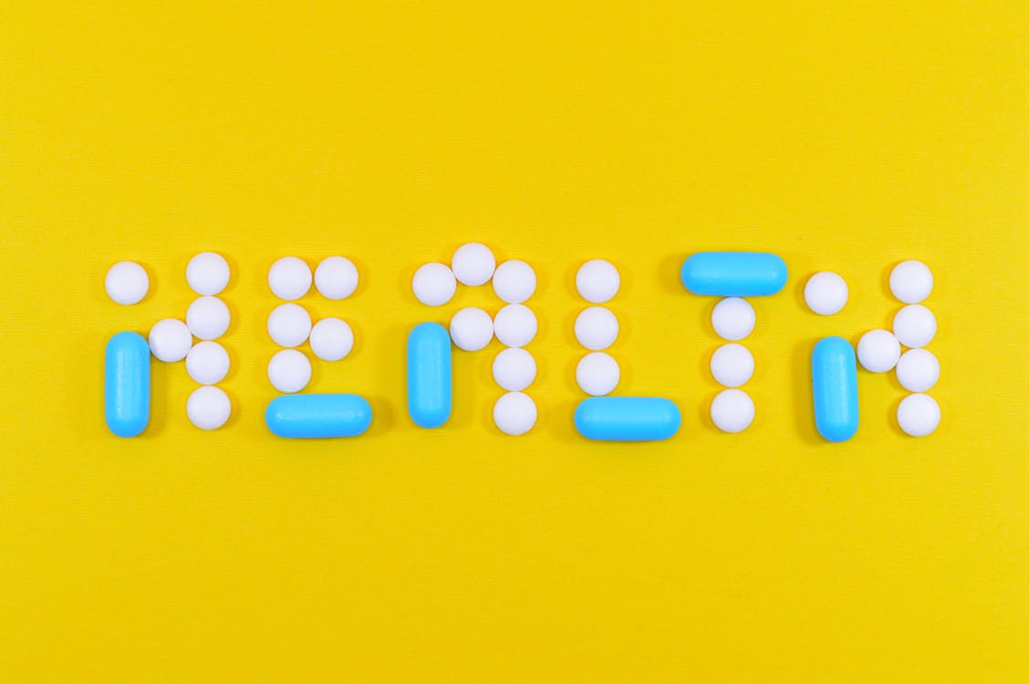 Free White and Blue Health Pill and Tablet Letter Cutout on Yellow Surface Stock Photo