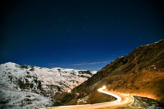 A scenic view of a snow-covered mountain road under a bright starry sky, captured at night.