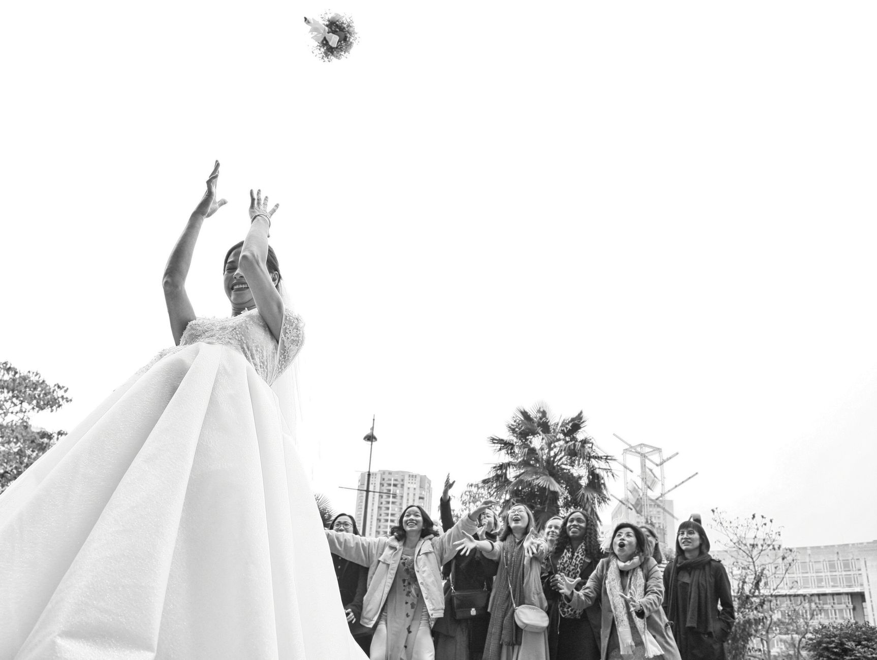 Une mariée lance son bouquet à des demoiselles d’honneur joyeuses, scène en noir et blanc à Paris.
