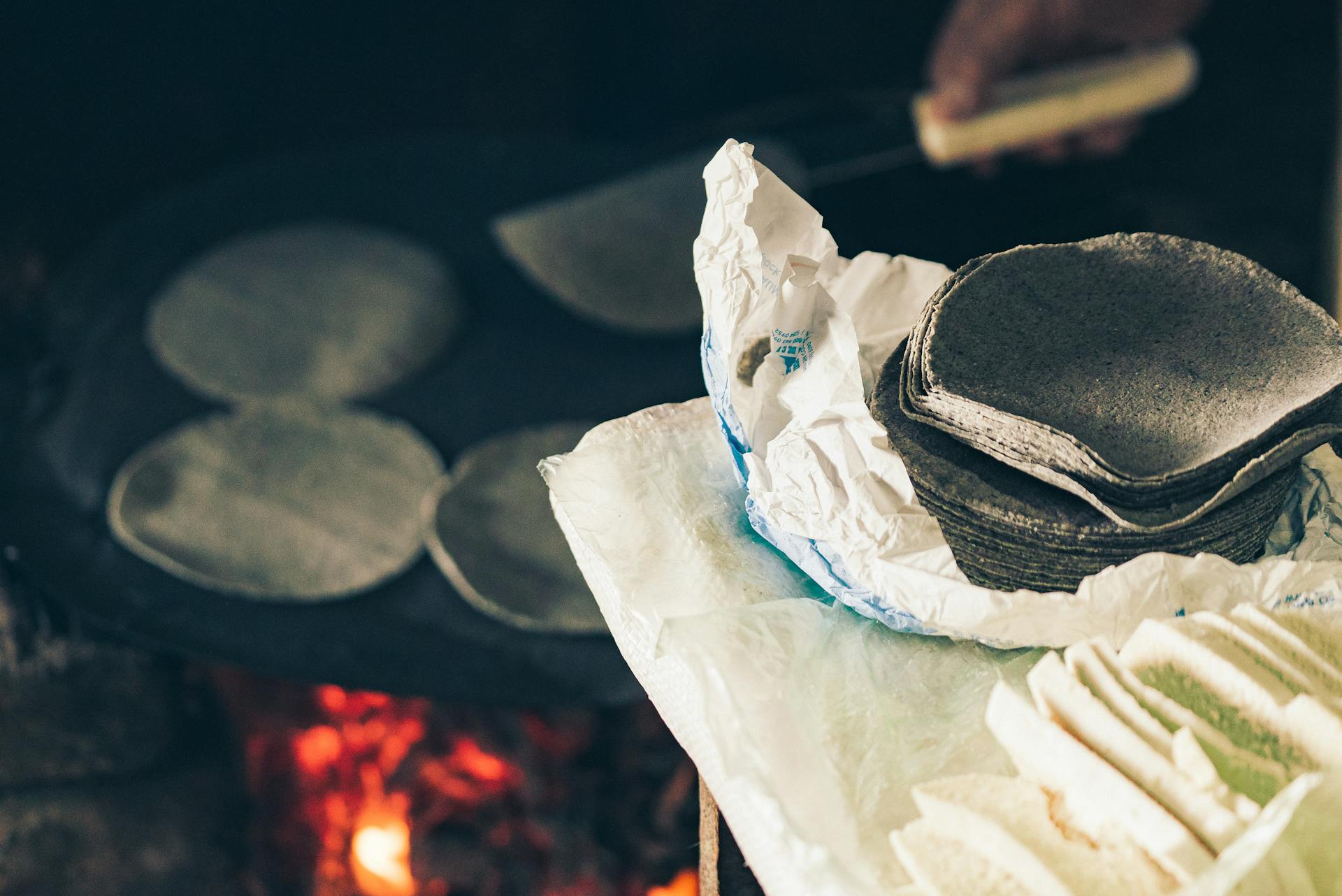 High angle of crop anonymous cook frying Mexican blue tortilla on fireplace near table with homemade cheese