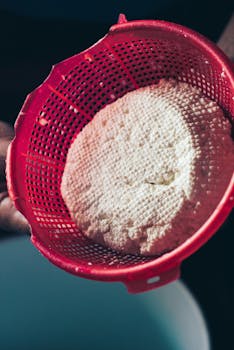 Close-up of homemade cottage cheese draining in a red sieve, showcasing its texture.